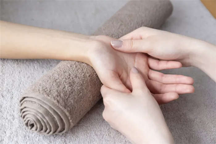 массаж кисти руки, лежащей на свернутом бежевом махровом полотенце